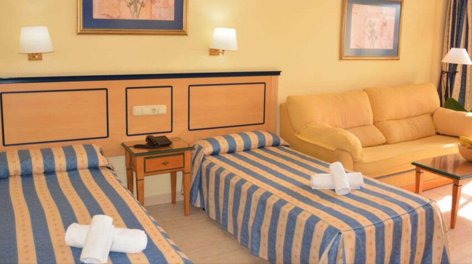 Habitación de hotel con dos camas, un sofá, una mesita y una lámpara.