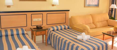 Habitación de hotel con dos camas, un sofá, una mesita y una lámpara.