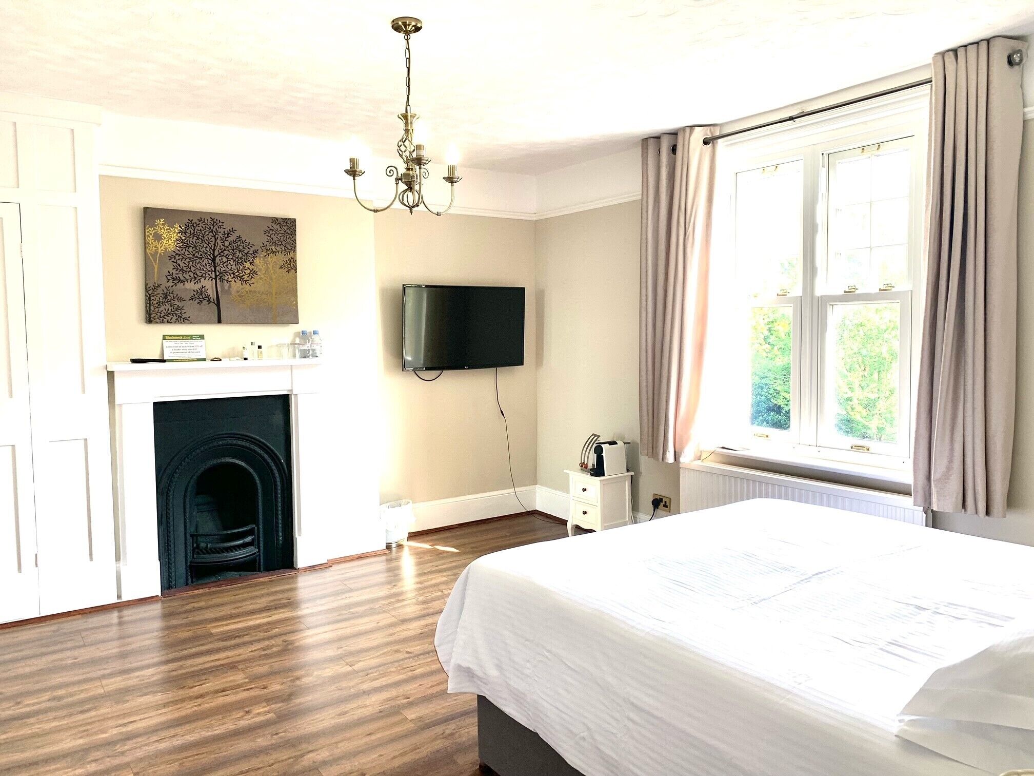 Un dormitorio con una cama grande, una chimenea, un televisor y un ventanal con cortinas.