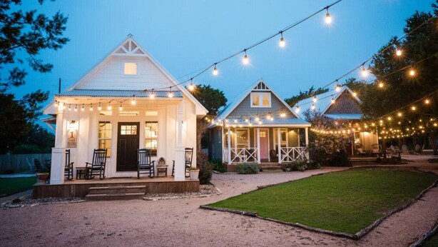 Deux charmantes maisons blanches dotées de vérandas, reliées par une guirlande de lumières.