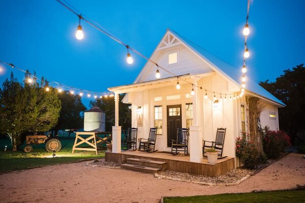 A white house with a porch and string lights, surrounded by trees and a tractor.