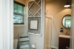 A bathroom with a shower, a toilet, a wicker basket, a toilet paper holder, and a mirror. - The Gruene Haus at Gruene B&B (New Braunfels)