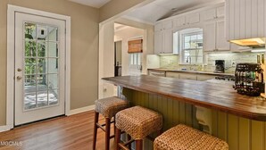 Una cocina con armarios blancos, una barra de madera y dos taburetes de mimbre.