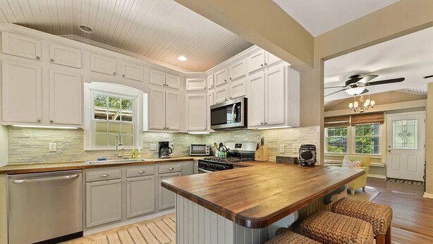 Una cocina con armarios blancos, una isla de madera y un ventilador de techo.