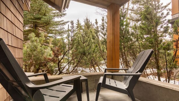 Un espacio de estar al aire libre cubierto con dos sillas Adirondack y una pequeña mesa, rodeado de árboles.