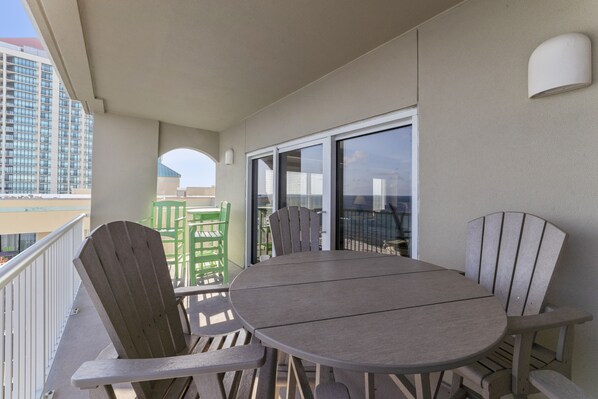 Un balcon avec une table ronde et des chaises, une vue sur un immeuble de grande hauteur et une porte vitrée donnant sur un espace extérieur.