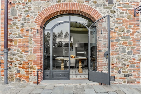 A stone building with a large arched entrance, a modern kitchen visible inside, and a metal door.