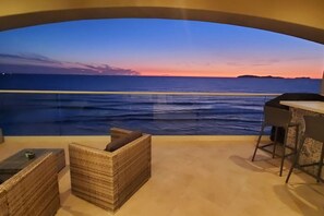 A room with a view of the sea at sunset, a small table, and a wicker chair. - BEACH FRONT CONDO, PRIVATE BEACH & AMAZING VIEWS!! (Rosarito)