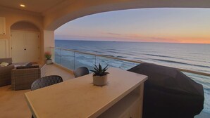 Ein Balkon mit Meerblick bei Sonnenuntergang, eine Sitzecke mit Tisch und ein Blumentopf.