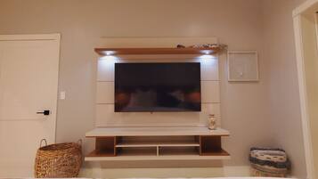 A room with a flat-screen TV mounted on a wooden shelf, a basket, and a small stool.