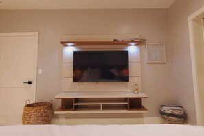 A room with a flat-screen TV mounted on a wooden shelf, a basket, and a small stool. - BEACH FRONT CONDO, PRIVATE BEACH & AMAZING VIEWS!! (Rosarito)