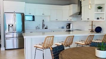 Cocina moderna con armarios blancos, electrodomésticos de acero inoxidable y una isla central con asientos.