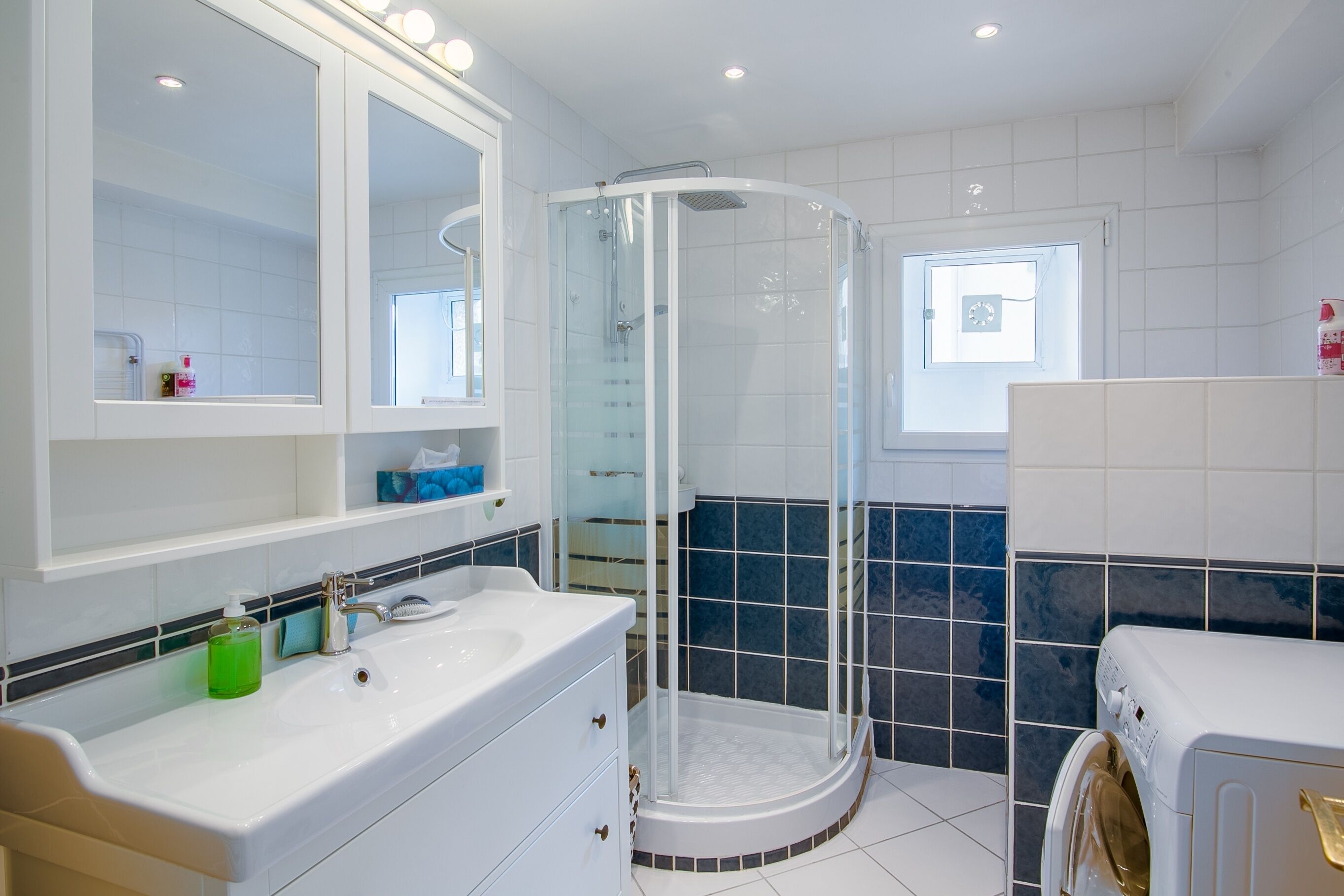 Ett modernt badrum med en duschavdelning med glasväggar, en vit tvättställ med en spegel ovanför och en inbyggd tvättmaskin.