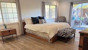 A bedroom with a wooden floor, a bed with a white bedspread, a zebra-patterned bench, and a wooden nightstand with a vase. - The Bluebird House Near Wineries Historic Downtown Murrieta  (Murrieta)