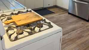 A modern kitchen with white cabinets, a stainless steel refrigerator, a microwave, and a gas stove with a wooden cutting board. - The Bluebird House Near Wineries Historic Downtown Murrieta  (Murrieta)