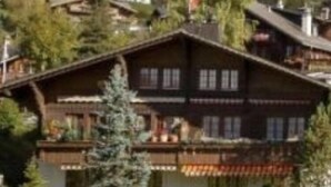 Un bâtiment de style chalet traditionnel, doté d’un toit en pente, entouré d’une végétation luxuriante et situé au pied d’une colline boisée.