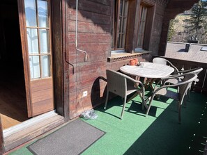 A wooden building with a patio area featuring a round table and wicker chairs. - Chalet Soldanella (Saanen)