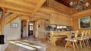 Un intérieur en bois comprenant un coin repas, des chaises en bois, une table et un plafond orné d’un lustre.