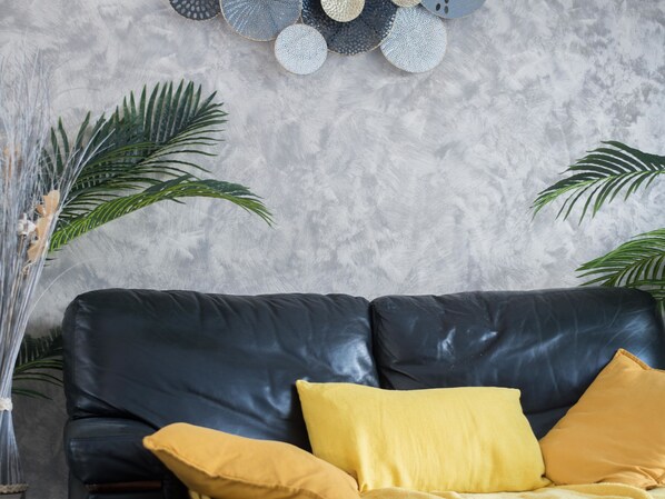 Un sofá de cuero negro con cojines amarillos, una pared gris con textura y un tapiz decorativo.