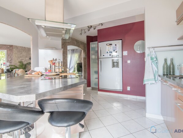 A modern kitchen with a central island, stainless steel appliances, and a red accent wall. - La Lilla - Piscine - Wifi (Chauve)