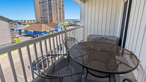 Un balcon avec une table et des chaises en métal, donnant sur un parking et un grand immeuble.