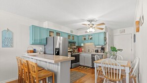 Une cuisine avec des armoires de couleur turquoise, un réfrigérateur en acier inoxydable, des chaises en bois et une table à manger.
