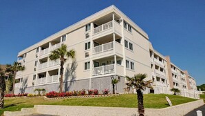 Un hôtel à plusieurs étages doté de balcons, d’un jardin clos et de palmiers.