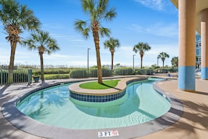 Swim in the tranquil pool surrounded by lush palm trees and a clear sky.
