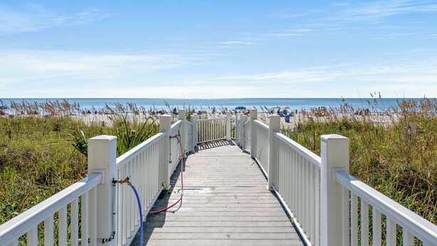 Een houten looppad dat naar een strand leidt, onder een heldere lucht.