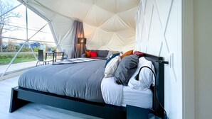 Un dormitorio de estilo tienda de campaña moderno, con cama, mesita de noche, lámpara y vistas al exterior.