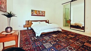 A bedroom with a large bed, a mirror, a rug, and a painting on the wall. - COLONEL'S ROOM (Cape Town)