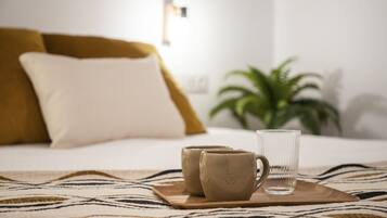 Una cama con una manta estampada de cebra, dos tazas color beige y un vaso transparente sobre una bandeja de madera.