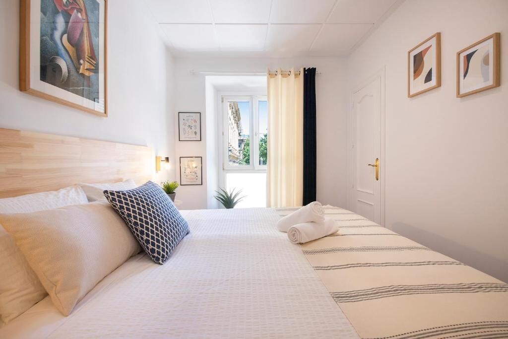 A hotel room with a bed, a window with curtains, and framed pictures on the wall.