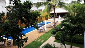 A pool area with a blue pool, lounge chairs, and a covered seating area. - Luxury apartment, 3 bedrooms (2 suites) - Praia da Espera - Itacimirim (Camaçari)