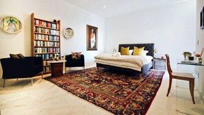 Een slaapkamer met een groot bed, een boekenplank, een bureau en een stoel.