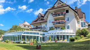 A large, multi-story hotel with a glass conservatory, outdoor seating, and a well-maintained garden. - Loft am Schluchsee (Schluchsee)