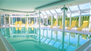 An indoor swimming pool with clear glass walls, yellow striped lounge chairs, and a view of greenery outside. - Loft am Schluchsee (Schluchsee)
