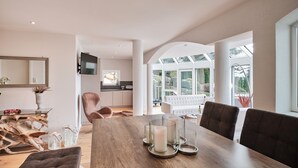 A spacious dining area with a wooden table, candles, and a view of the kitchen and garden through large windows. - Loft am Schluchsee (Schluchsee)