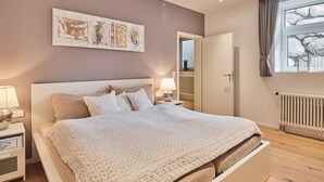 A bedroom with a large bed, a nightstand, a lamp, a radiator, and a window with curtains. - Loft am Schluchsee (Schluchsee)