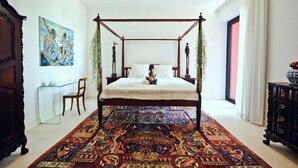 Uma cama de dossel com um tapete estampado, um quadro na parede e uma escrivaninha com cadeiras.