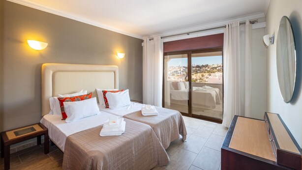 Una camera d'albergo con due letti, un balcone con vista sulla città, una scrivania e uno specchio.