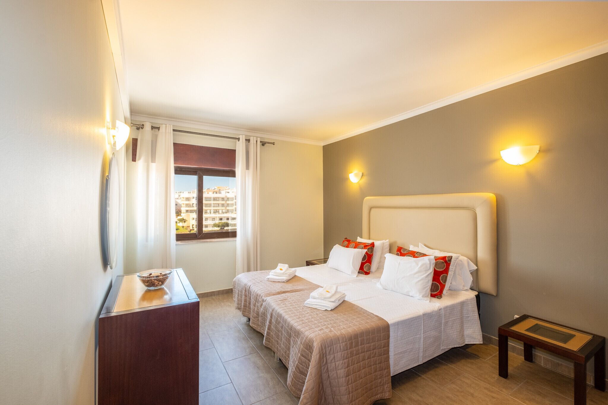 Une chambre d’hôtel avec deux lits, une petite table, une fenêtre avec des rideaux et une vue sur les bâtiments environnants.