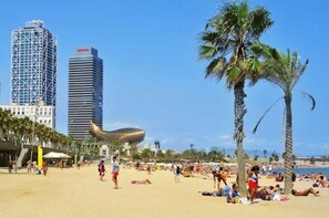 A beach with palm trees and people sunbathing. There are tall buildings in the background.