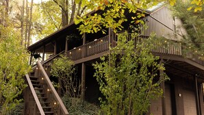 Eine Holzhütte mit einer Treppe, die zu einer Terrasse führt, umgeben von dichtem Grün.