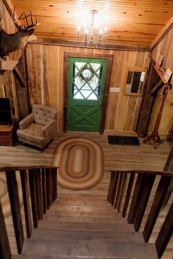 A wooden interior with a green door, a tufted armchair, a chandelier, and a mounted deer head.