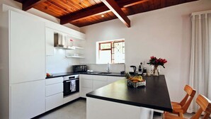 A modern kitchen with white cabinetry, a black countertop, and wooden chairs. - CAPTAIN'S COTTAGE (Cape Town)