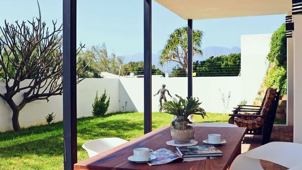 An outdoor patio with a wooden table, chairs, and a white umbrella. - CAPTAIN'S COTTAGE (Cape Town)