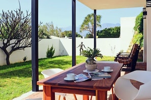 An outdoor patio with a wooden table, chairs, and a white umbrella. - CAPTAIN'S COTTAGE (Cape Town)