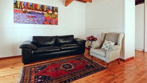 A living room with a black leather sofa, a patterned rug, a checkered armchair, and a painting on the wall. - ADMIRAL'S COTTAGE (Cape Town)