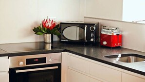 A kitchen with a microwave, toaster, and a small plant on the counter. - ADMIRAL'S COTTAGE (Cape Town)